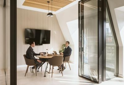 Two professionals in a focused discussion at a round wooden table in a private office suite.