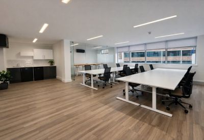 Open-plan workspace with white desks, ergonomic chairs, and a sleek kitchenette.