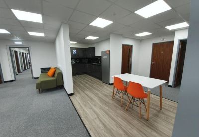 Communal breakout area with an olive green sofa, orange chairs, and a kitchen corner.
