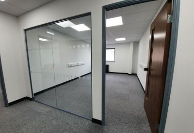 View into a bright, private office through a glass partition and an open wooden door.