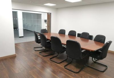 Boardroom with a long wood-effect table, black chairs, and dark wood flooring.