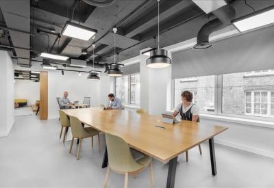 Large wooden communal desk in a bright room with industrial black ceilings.