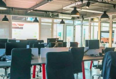 Bright open-plan office with rows of desks, computer monitors, and modern pendant lights.