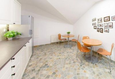 Communal kitchen and dining area with round tables, orange chairs, and stone tile flooring.