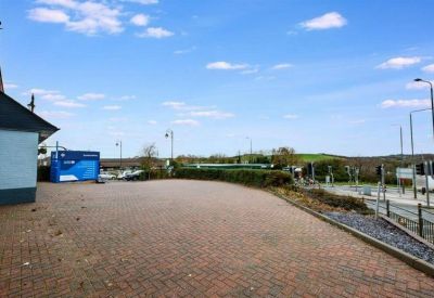 Paved exterior parking area under a blue sky with surrounding greenery and distant hills.