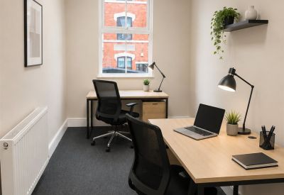 Narrow two-person office with desks facing a large window overlooking a red brick building.