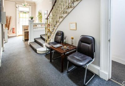 Waiting area in a hallway with two leather chairs and a dark wood side table next to a staircase.