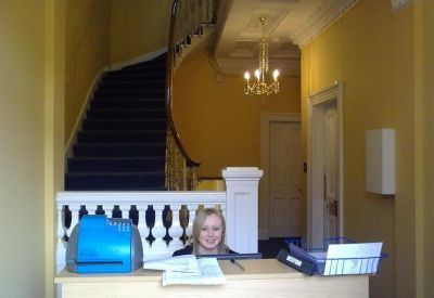 Reception desk featuring a bright blue printer and classic architectural staircase with wood bannisters.