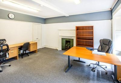 Bright office space with two wooden desks, ergonomic chairs, and a decorative fireplace.