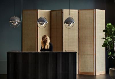 Reception area with a dark fluted desk, wooden folding screen, and globe pendant lighting.