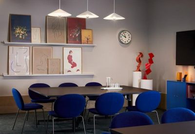 Meeting room with a long dark table, vibrant blue chairs, and a gallery wall of framed art.