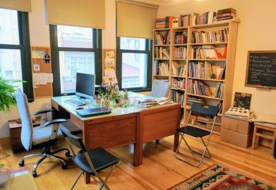 Bright office space with two desks, computers, and floor-to-ceiling bookshelves.