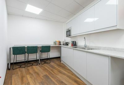 Communal kitchen and break area with white cabinetry and green velvet bar stools.