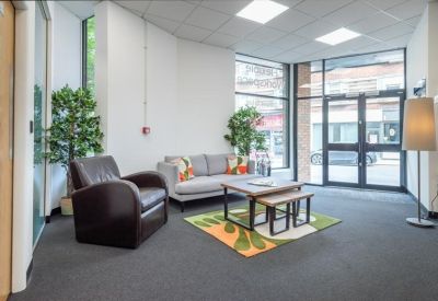 Modern reception lounge with a grey sofa, brown armchair, and colorful patterned rug.