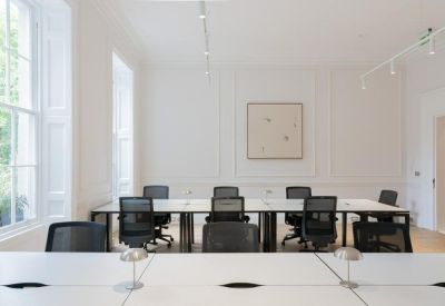 Modern open-plan office with rows of white desks and black ergonomic chairs.