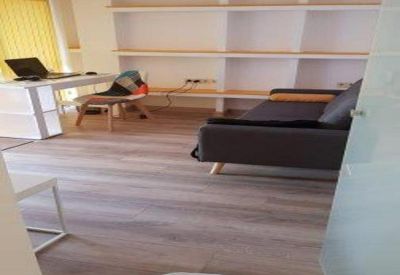 Open office area featuring a dark sofa, wooden floors, and built-in white shelving.