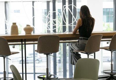 Coworking cafe area with high stools along a wooden bar overlooking a large window.