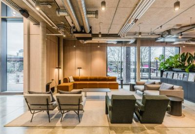 Spacious lounge area with industrial ceilings, plush seating, and indoor plants.