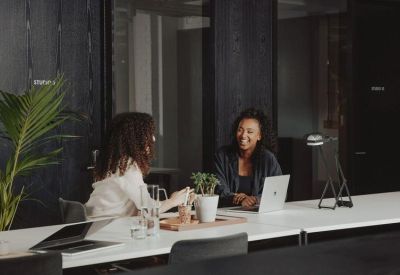 Two people working and talking at a long white shared office desk.