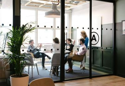 Glass-walled meeting room with professionals collaborating around a table.