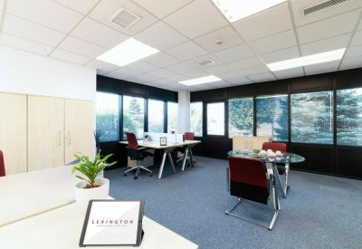 Bright open-plan office space featuring modular white desks and dark grey carpeting.