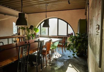 Bright coworking space with a long wooden desk and sunlight streaming through an arched window.