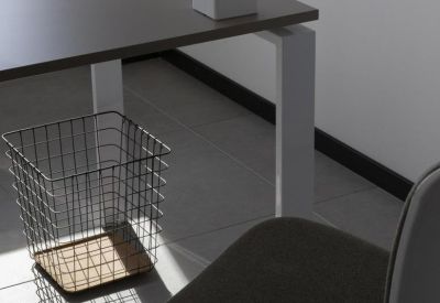 Close-up of a desk with a grey surface and wire waste basket.