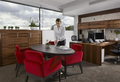 Private office suite with a dark wood meeting table, red velvet chairs, and large window.