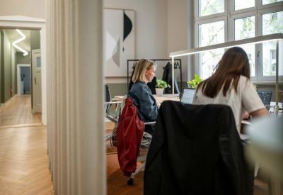Coworking space with people working at desks near a bright window.