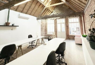 Bright coworking space with skylights, exposed brick, and long rows of white desks.