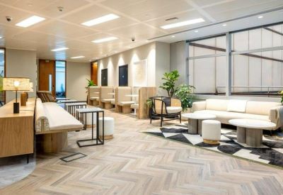 Bright communal lounge with cream sofas, wooden herringbone floors, and modern circular coffee tables.