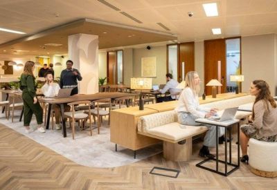 Open-plan coworking space with a central wooden pillar, laptop workstations, and people collaborating.