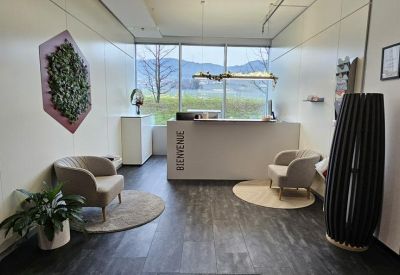 Bright reception area with a white desk, comfortable armchairs, and a green wall feature.