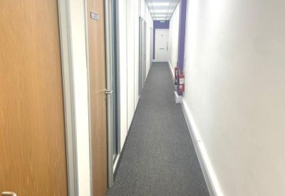 Long bright hallway with grey carpeting and several light wood doors.