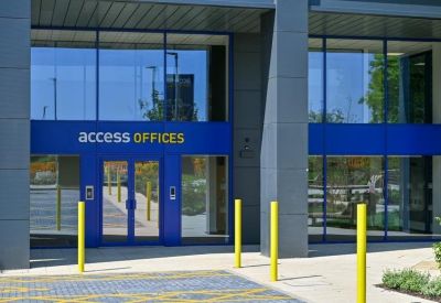 Modern glass entrance with blue accents and yellow bollards.