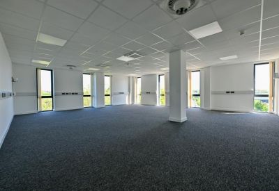 Spacious open-plan office space with grey carpeting and large windows.