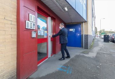 Man in a suit opening a red-framed glass door with a keypad entry system.