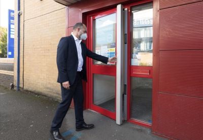 Close-up of a person entering a secure red door with silver vertical handles.