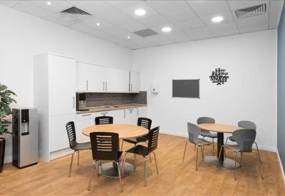 Communal break area with a white kitchenette, dining tables, and wood-style flooring.