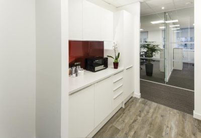 Modern office kitchenette with white cabinetry, wood-style flooring, and a glass partition.