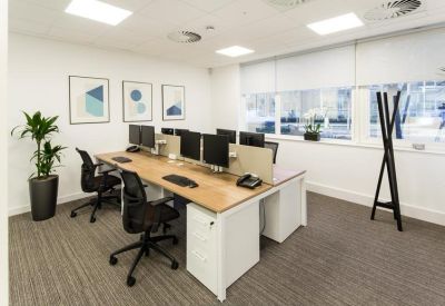 Bright open-plan office with wooden desks, ergonomic chairs, and framed wall art.
