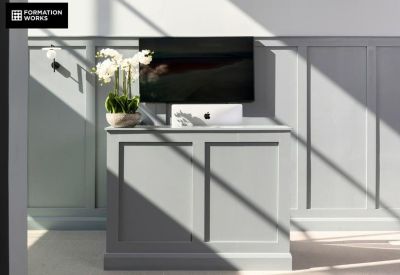 Minimalist reception or side desk with a monitor and orchid plant against a paneled wall.