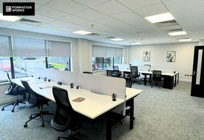 Spacious open-plan workspace with white desks and black ergonomic chairs.