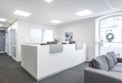 Minimalist white reception desk in a bright lobby with a grey sofa and large arched window.