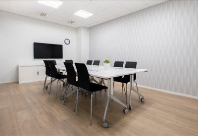 Modern conference room featuring a long white table, black chairs, and a wall-mounted screen.