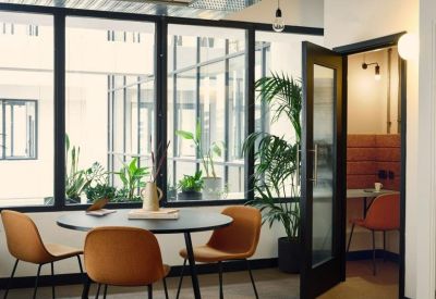 Bright glass-walled break area with circular table, orange chairs, and potted greenery.