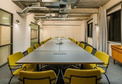 Professional boardroom with a long grey table and vibrant yellow chairs under industrial ceilings.