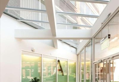 Bright glass-roofed corridor with white beams and indoor potted plant.