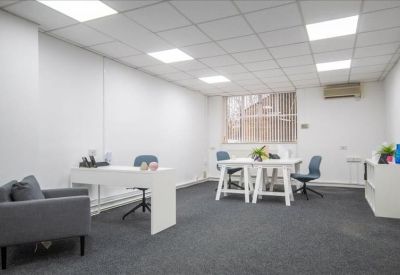 Bright private office suite with two white desks, grey armchairs, and large windows.