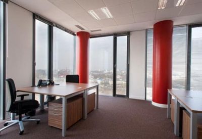 Bright corner office with wooden desks, ergonomic chairs, and floor-to-ceiling windows featuring red columns.